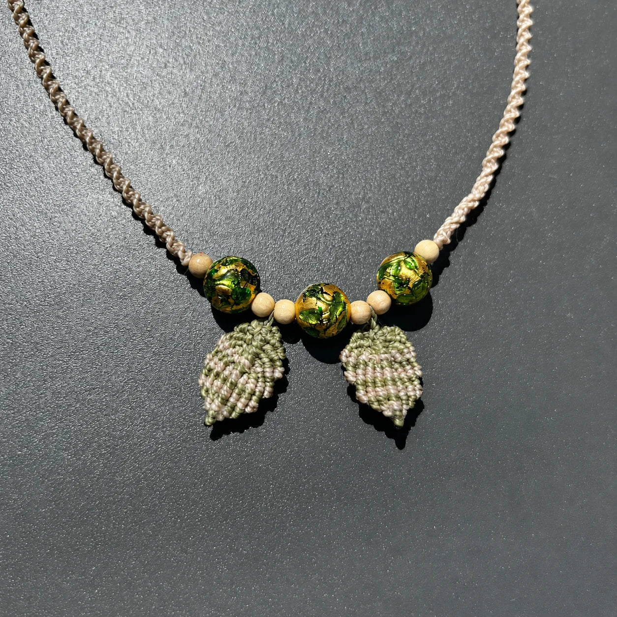 collier macramé motif feuille et perles de verre posé sur un fond gris foncé
