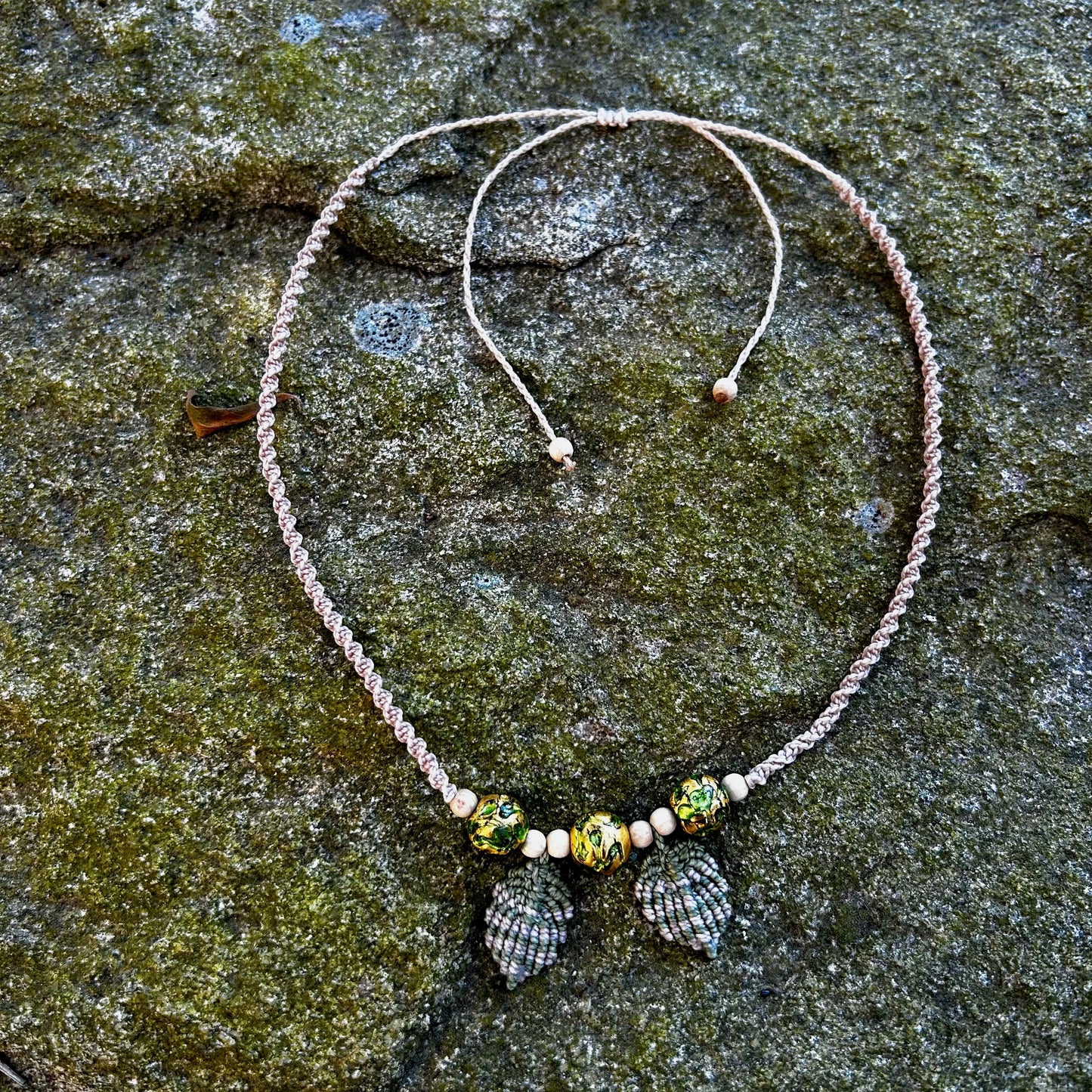 collier macramé feuilles et perles de verre vert et or posé sur un rocher