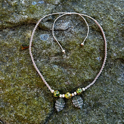 collier macramé feuilles et perles de verre vert et or posé sur un rocher