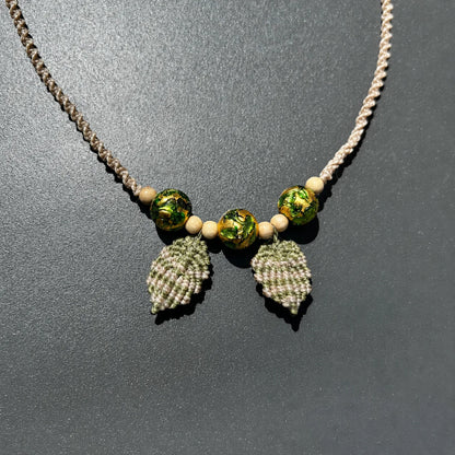 collier macramé motif feuille et perles de verre posé sur un fond gris foncé