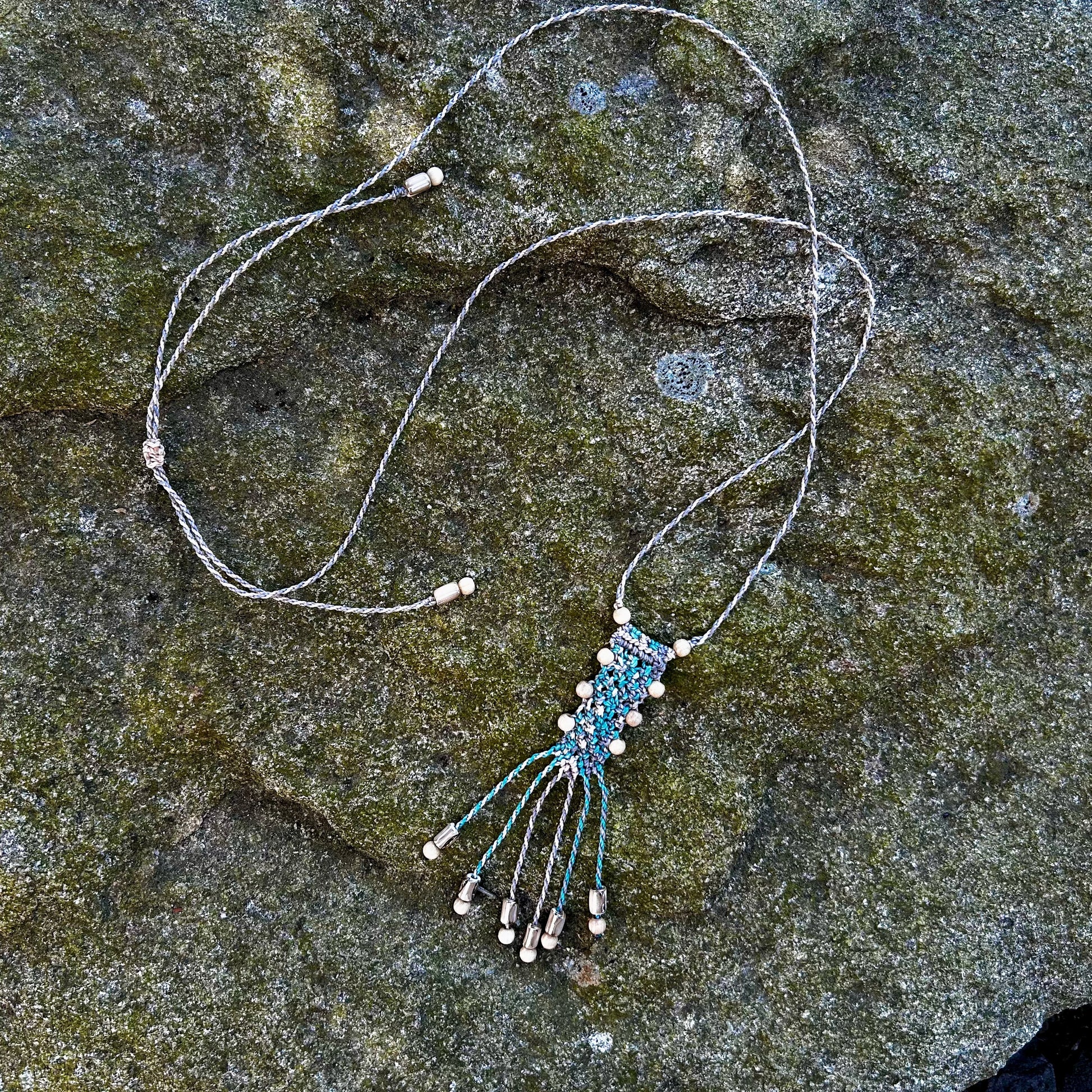 Collier en macramé et perles de bois posé sur un rocher
