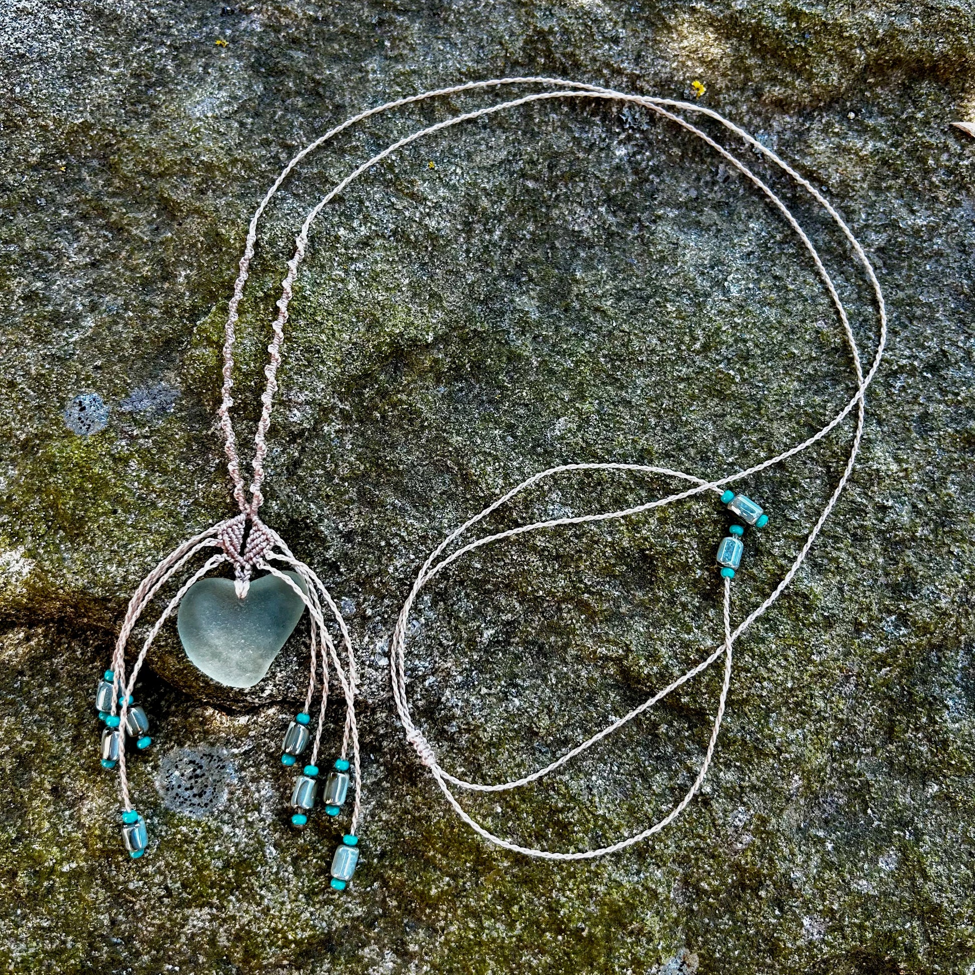 Collier macramé et verre de mer posé sur un rocher