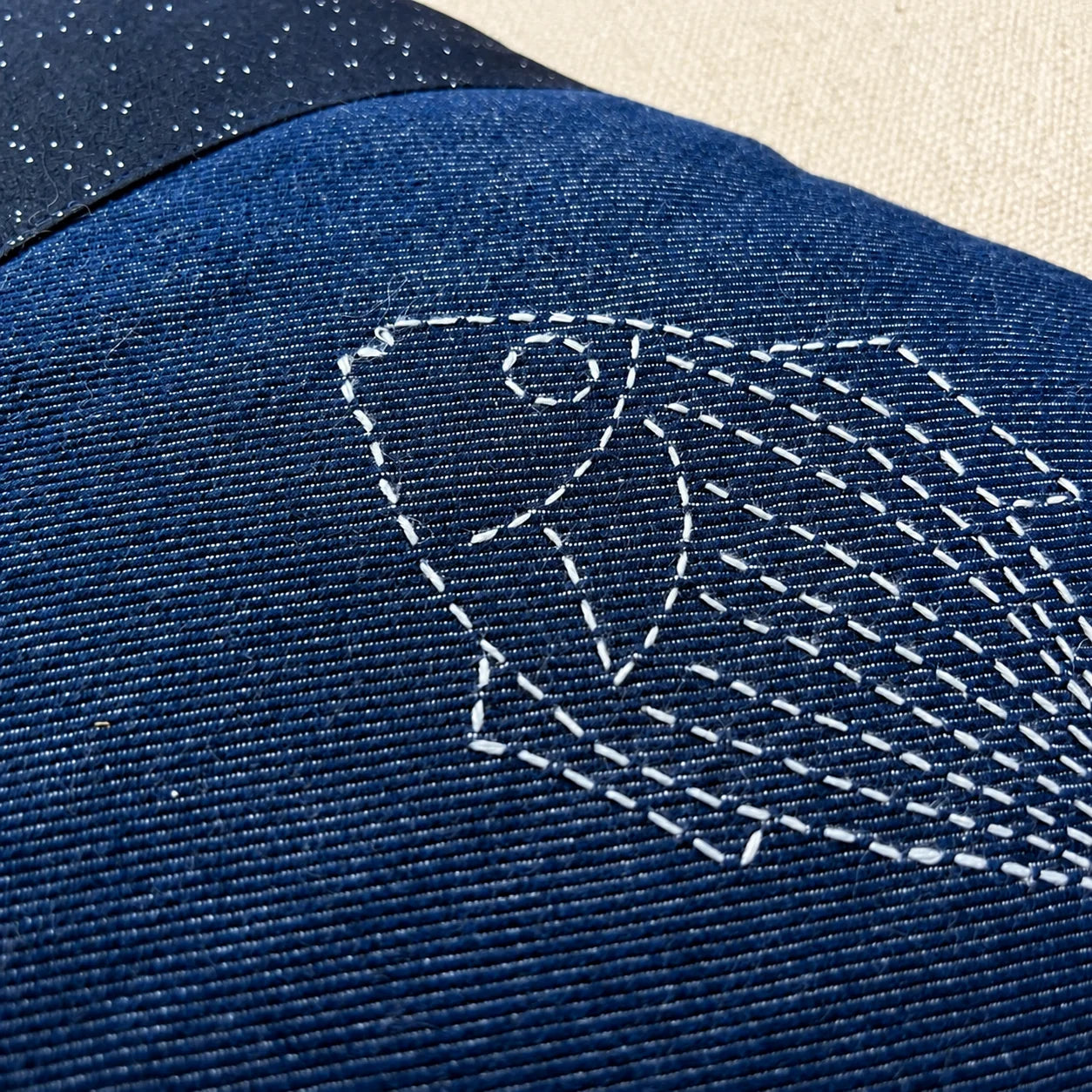 Détail d’un poisson brodé au sashiko blanc sur le denim bleu du coussin Les Deux Poissons