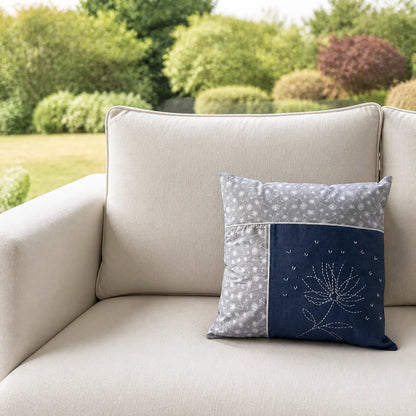 Coussin Fleur de Printemps brodé posé sur un canapé écru devant un jardin flouté