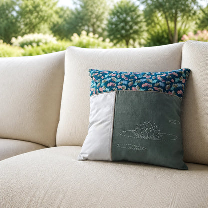Coussin Nénuphar brodé posé sur un canapé écru devant un jardin flouté