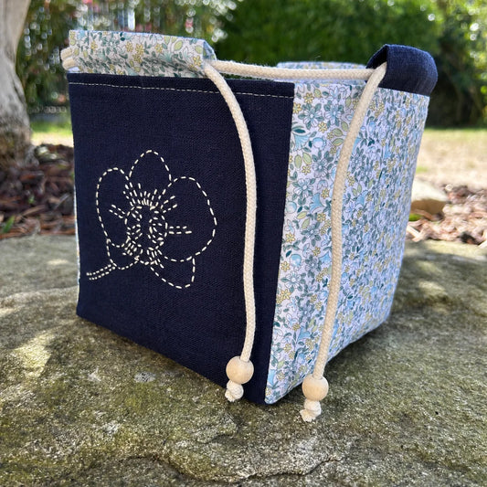 sac brodé orchidée posé sur une pierre